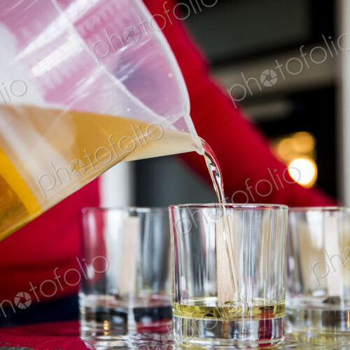 Close up of person pouring liquid wax for handmade candles into glass jars.