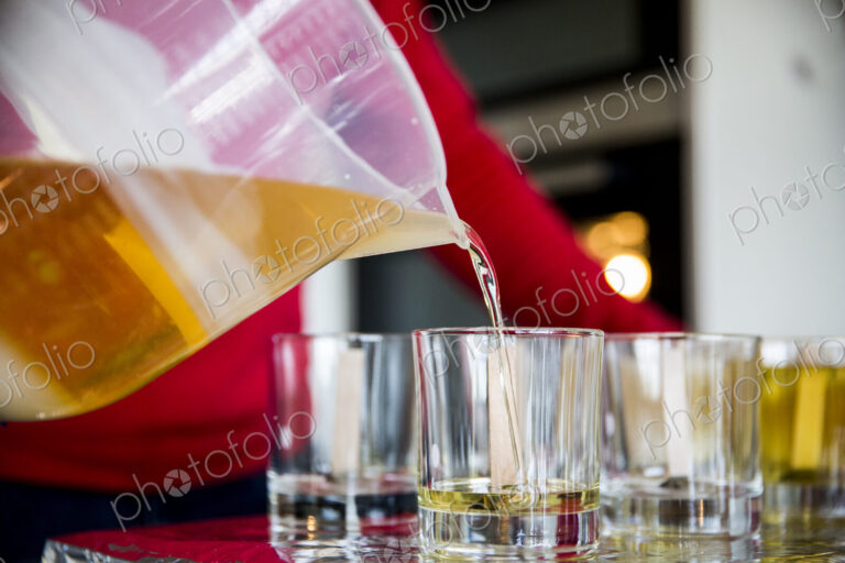 Close up of person pouring liquid wax for handmade candles into glass jars.