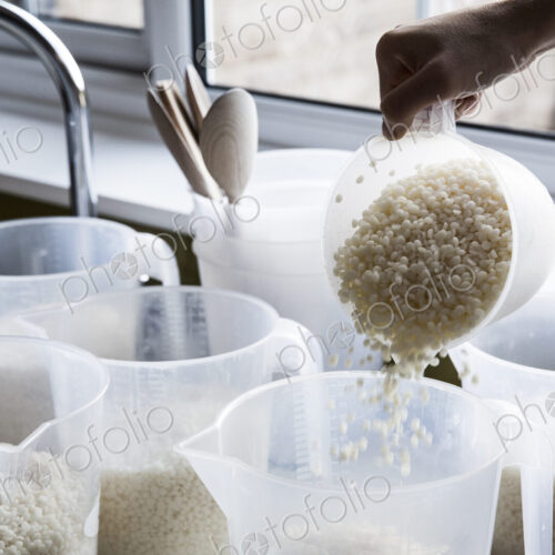 Close up of person pouring wax granules for handmade candles into jugs.