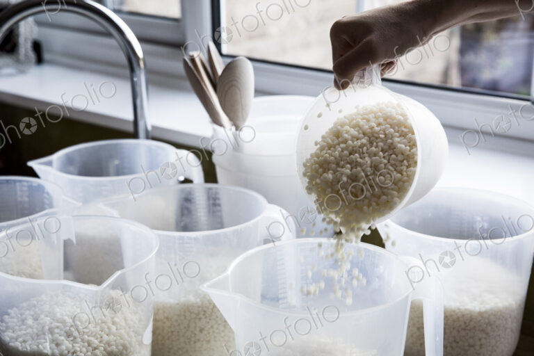 Close up of person pouring wax granules for handmade candles into jugs.