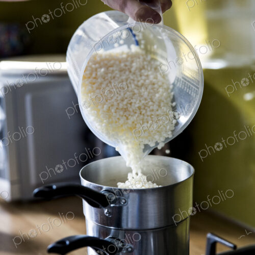 Close up of person pouring wax granules for handmade candles into saucepan for melting.