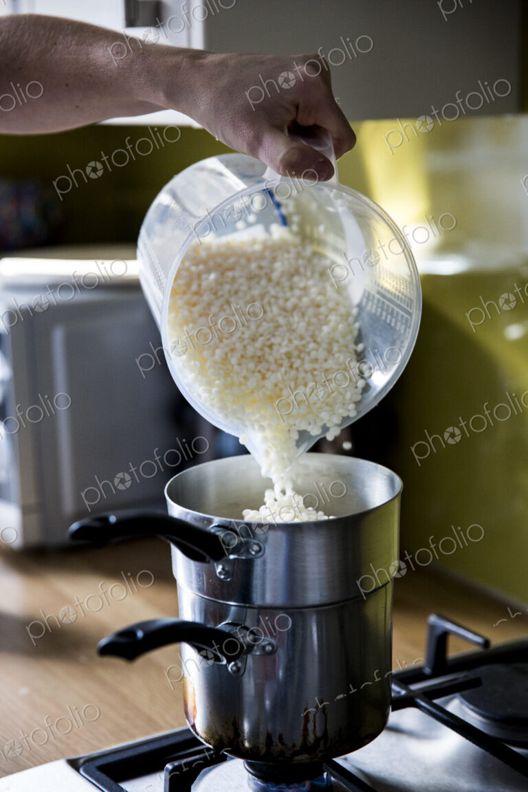 Close up of person pouring wax granules for handmade candles into saucepan for melting.