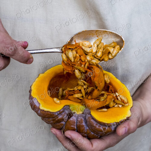 Close up of person using silver tablespoon to remove seed from a pumpkin.