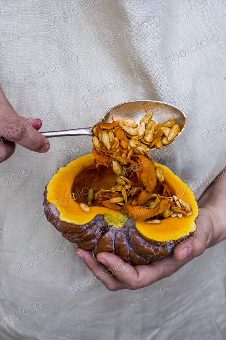 Close up of person using silver tablespoon to remove seed from a pumpkin.