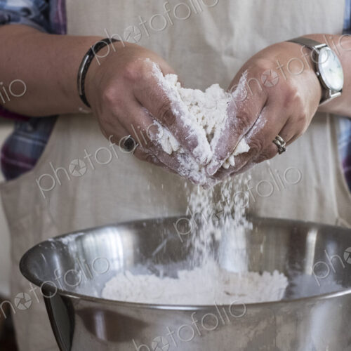 Close up of person wearing apron standing in kitchen, mixing ingredients for a crumble…