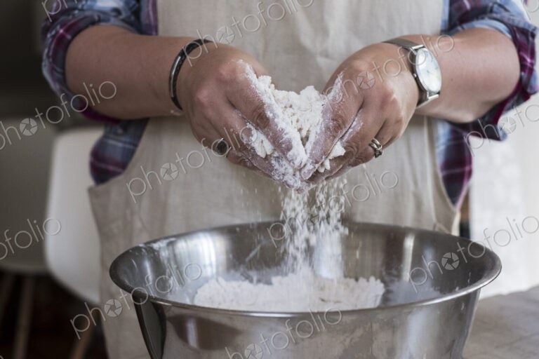 Close up of person wearing apron standing in kitchen, mixing ingredients for a crumble…