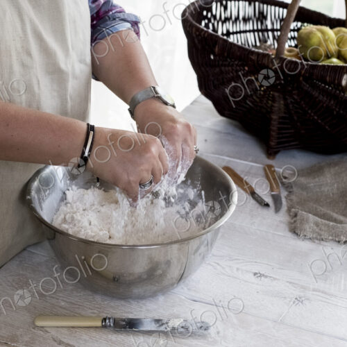 Close up of person wearing apron standing in kitchen, mixing ingredients for a crumble…