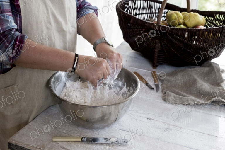 Close up of person wearing apron standing in kitchen, mixing ingredients for a crumble…