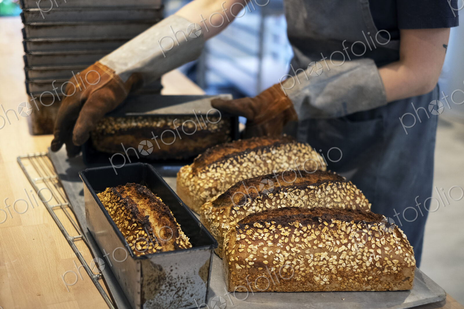 Close up of person wearing oven gloves placing freshly baked seeded loaves of bread on…