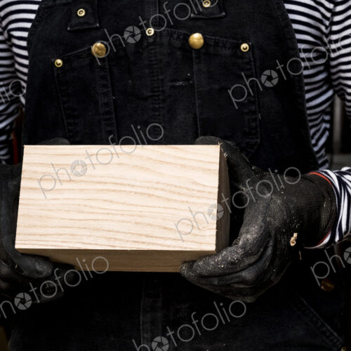 Close up of person wearing protective gloves holding wooden block. Close up of person wearing protective gloves holding wooden block.