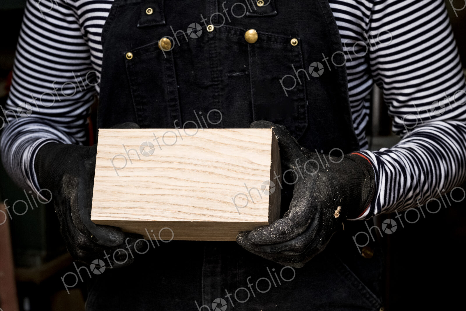 Close up of person wearing protective gloves holding wooden block.