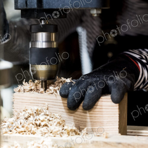 Close up of person wearing protective gloves using electric drill in wood workshop. Close up of person wearing protective gloves using electric drill in wood workshop.