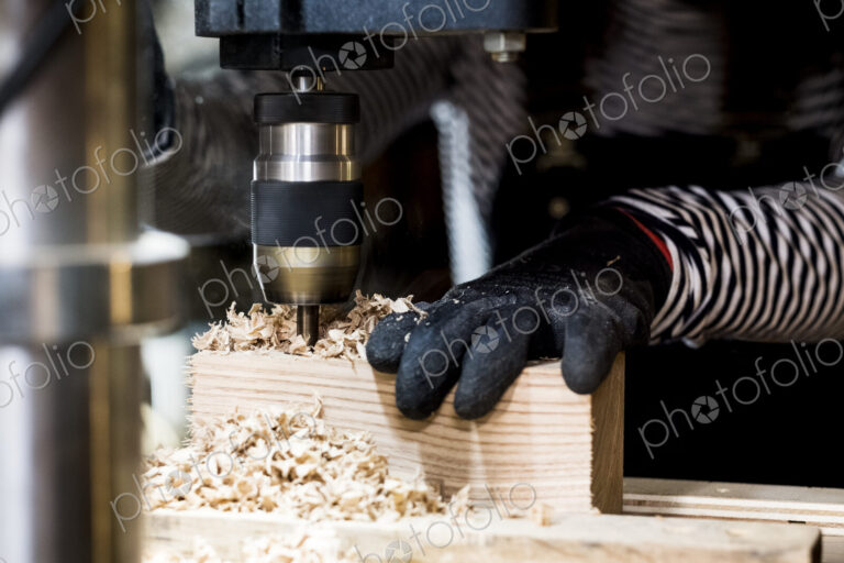 Close up of person wearing protective gloves using electric drill in wood workshop.