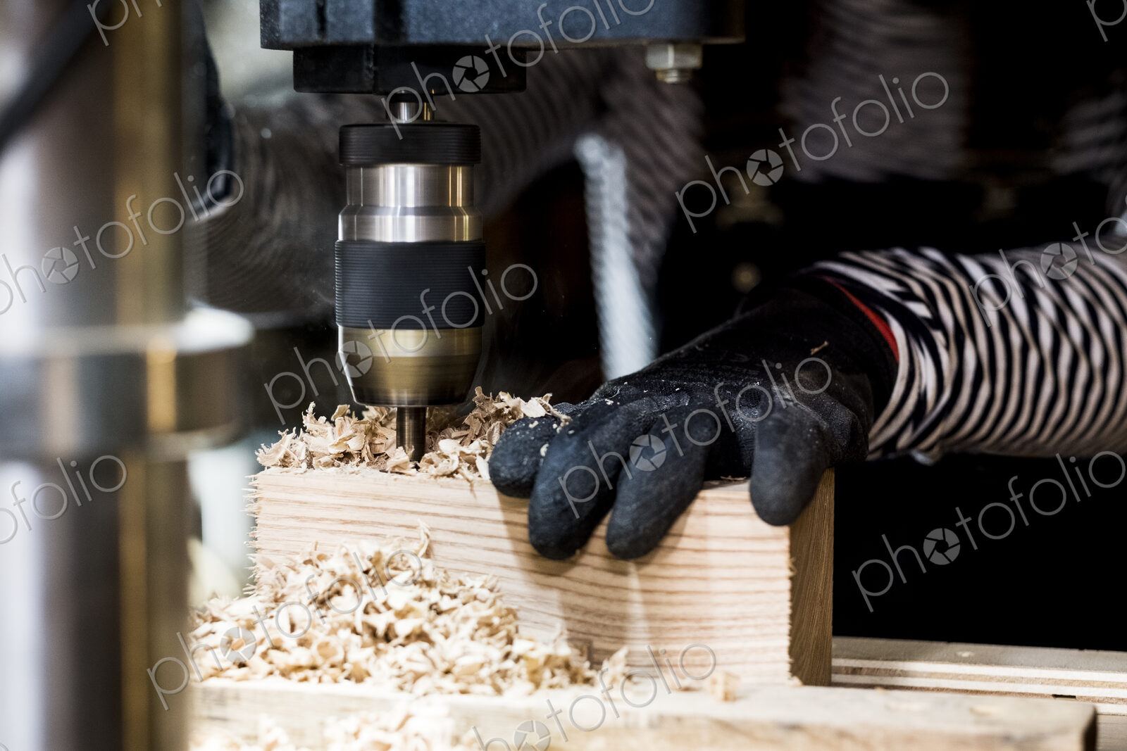 Close up of person wearing protective gloves using electric drill in wood workshop.