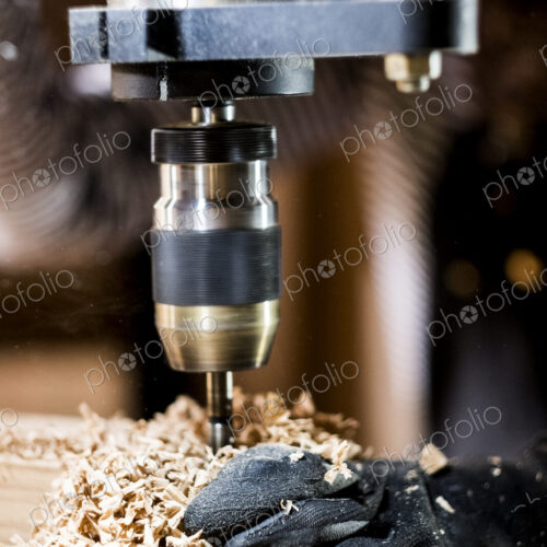 Close up of person wearing protective gloves using electric drill in wood workshop. Close up of person wearing protective gloves using electric drill in wood workshop.