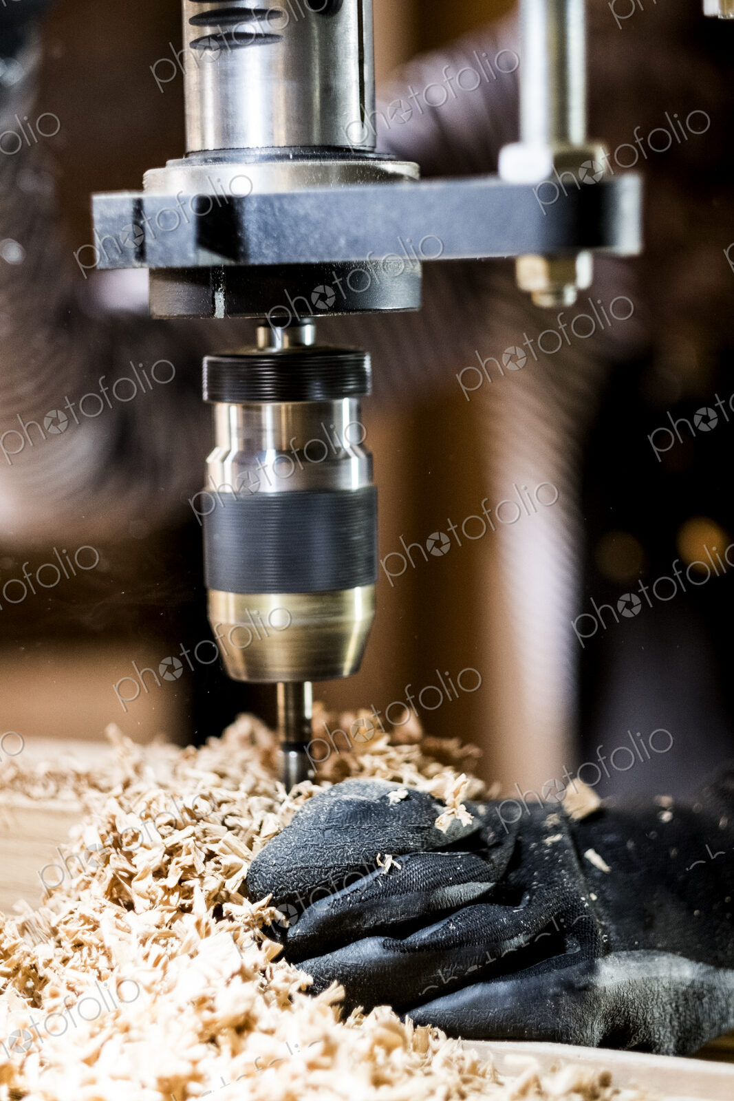 Close up of person wearing protective gloves using electric drill in wood workshop.