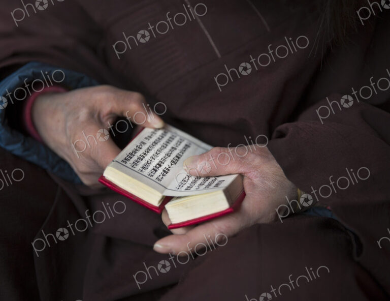 Close up of person wearing purple robe, holding prayer book in hands.