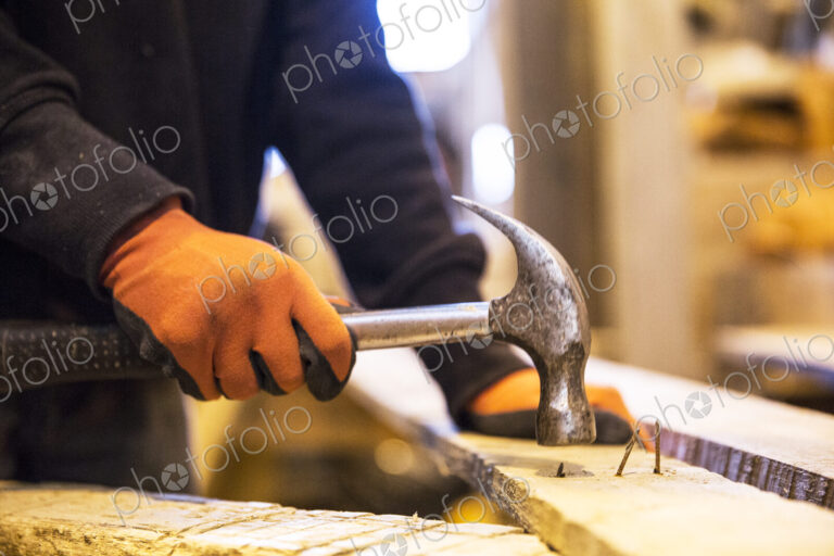 Close up of person wearing work gloves holding, hammer, removing rusty nails from…
