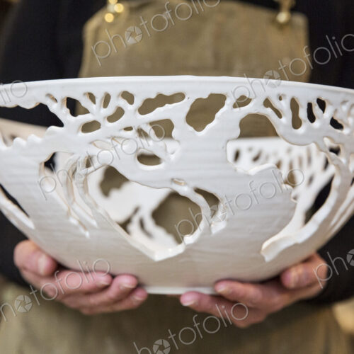 Close up of potter wearing apron holding a large intricate white ceramic bowl. Close up of potter wearing apron holding a large intricate white ceramic bowl.