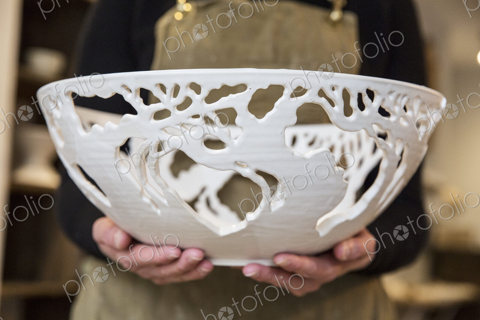 Close up of potter wearing apron holding a large intricate white ceramic bowl.