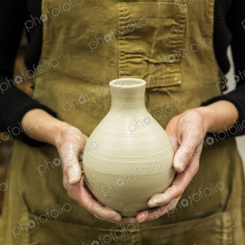 Close up of potter wearing apron holding unfired spherical clay vase. Close up of potter wearing apron holding unfired spherical clay vase.