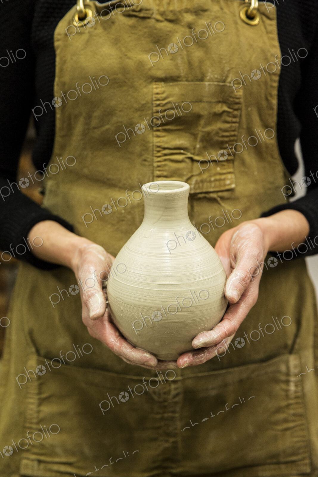 Close up of potter wearing apron holding unfired spherical clay vase.