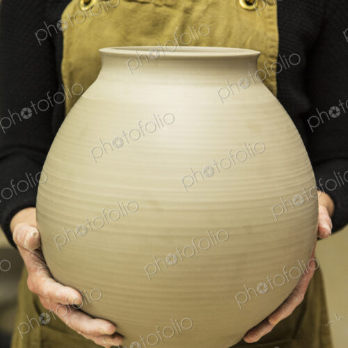 Close up of potter wearing apron holding unfired spherical clay vase. Close up of potter wearing apron holding unfired spherical clay vase.