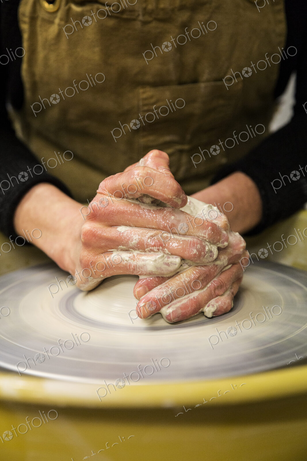 Close up of potter wearing apron working on pottery wheel, shaping clay.