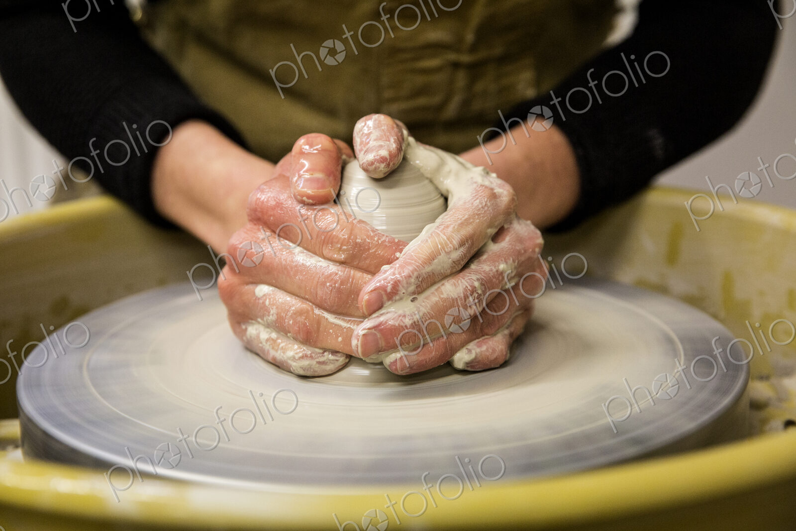 Close up of potter wearing apron working on pottery wheel, shaping clay.