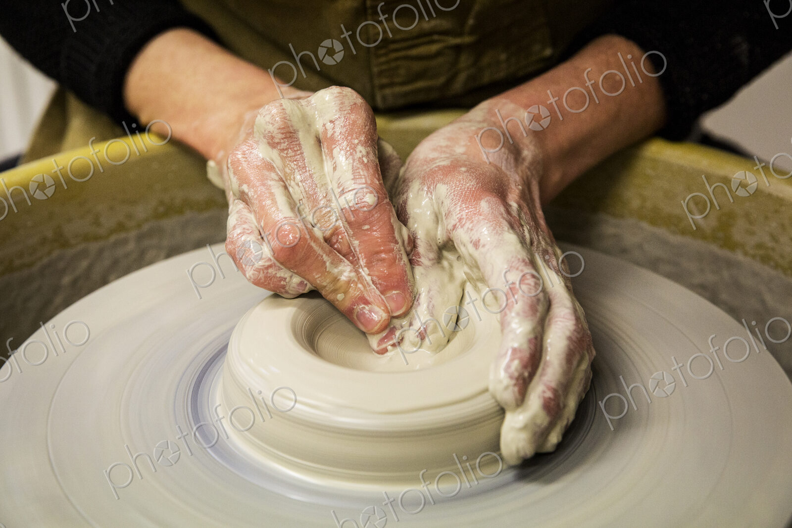 Close up of potter wearing apron working on pottery wheel, shaping clay vase.
