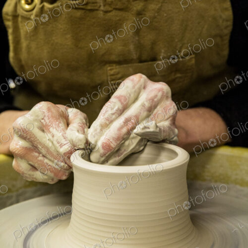 Close up of potter wearing apron working on pottery wheel, shaping clay vase. Close up of potter wearing apron working on pottery wheel, shaping clay vase.