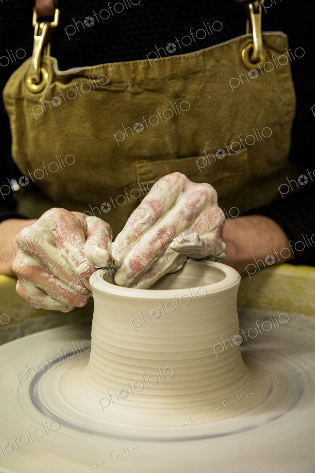 Close up of potter wearing apron working on pottery wheel, shaping clay vase.
