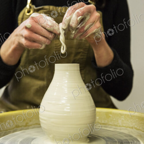 Close up of potter wearing apron working on pottery wheel, shaping clay vase. Close up of potter wearing apron working on pottery wheel, shaping clay vase.