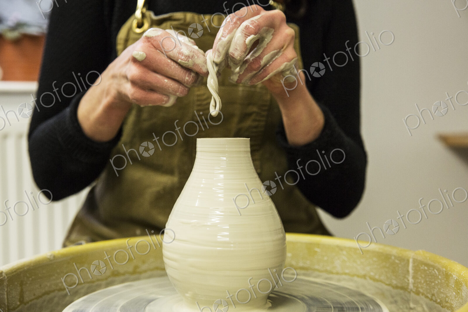 Close up of potter wearing apron working on pottery wheel, shaping clay vase.