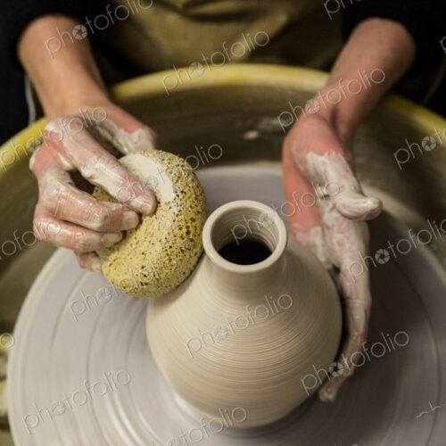 Close up of potter wearing apron working on pottery wheel, shaping clay vase. Close up of potter wearing apron working on pottery wheel, shaping clay vase.