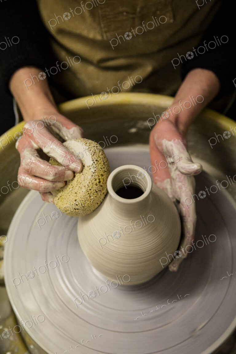 Close up of potter wearing apron working on pottery wheel, shaping clay vase.