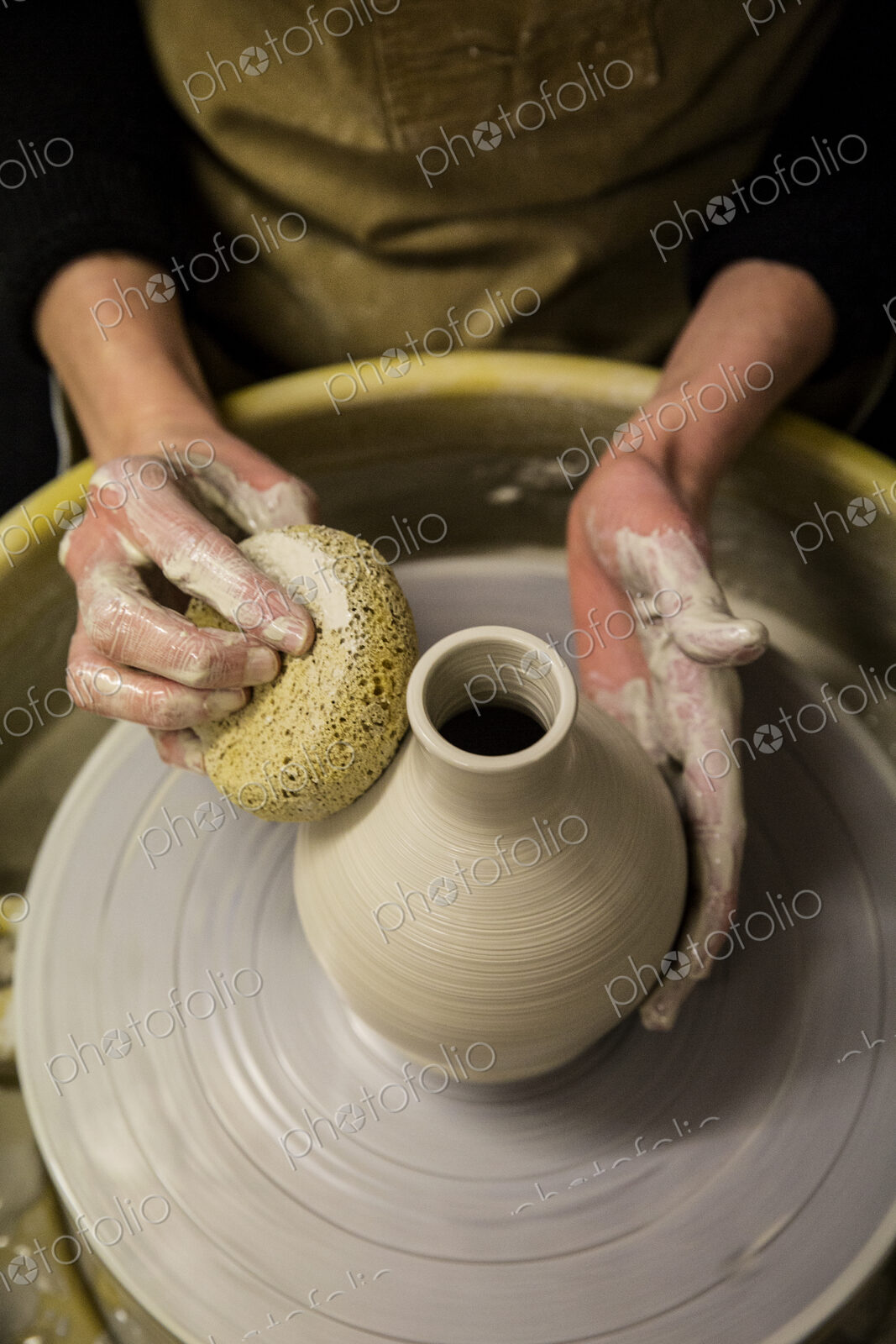 Close up of potter wearing apron working on pottery wheel, shaping clay vase.
