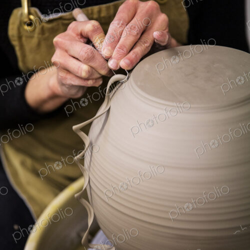Close up of potter wearing apron working on spherical clay vase on pottery wheel. Close up of potter wearing apron working on spherical clay vase on pottery wheel.