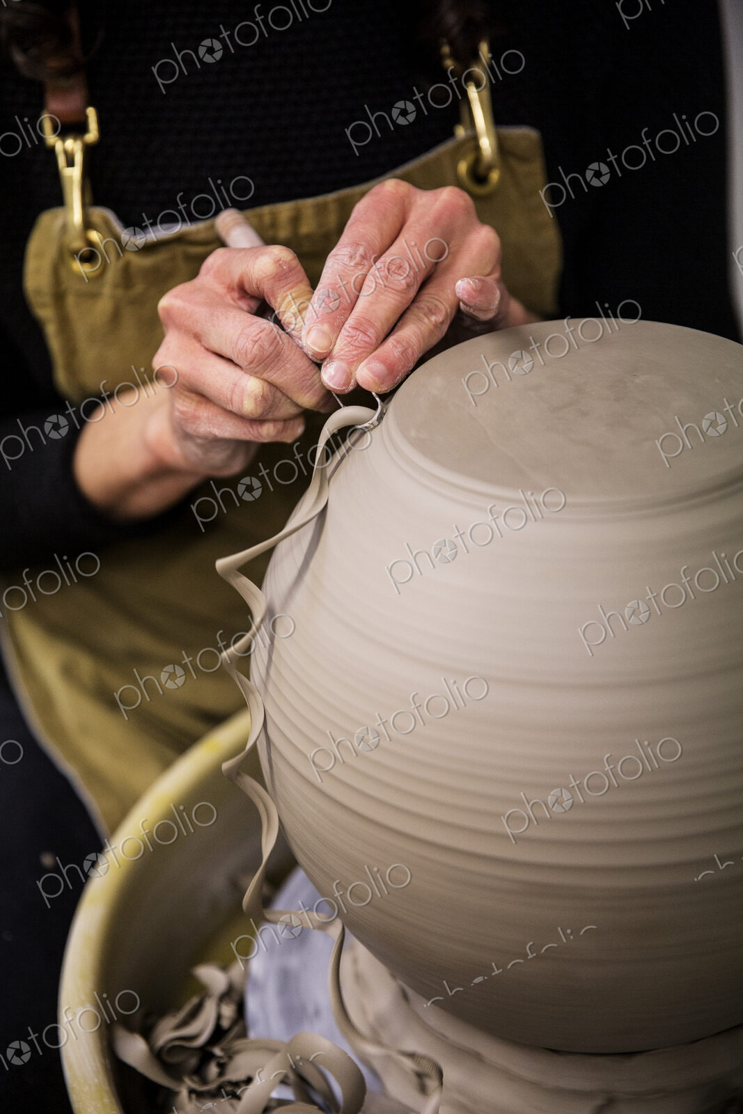 Close up of potter wearing apron working on spherical clay vase on pottery wheel.