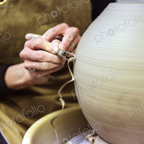 Close up of potter wearing apron working on spherical clay vase on pottery wheel. Close up of potter wearing apron working on spherical clay vase on pottery wheel.