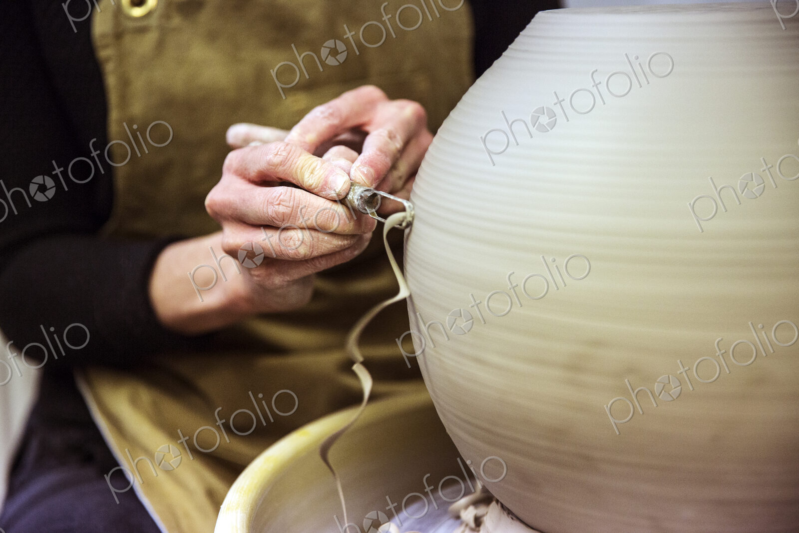 Close up of potter wearing apron working on spherical clay vase on pottery wheel.