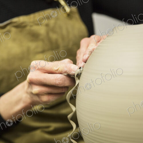Close up of potter wearing apron working on spherical clay vase on pottery wheel. Close up of potter wearing apron working on spherical clay vase on pottery wheel.