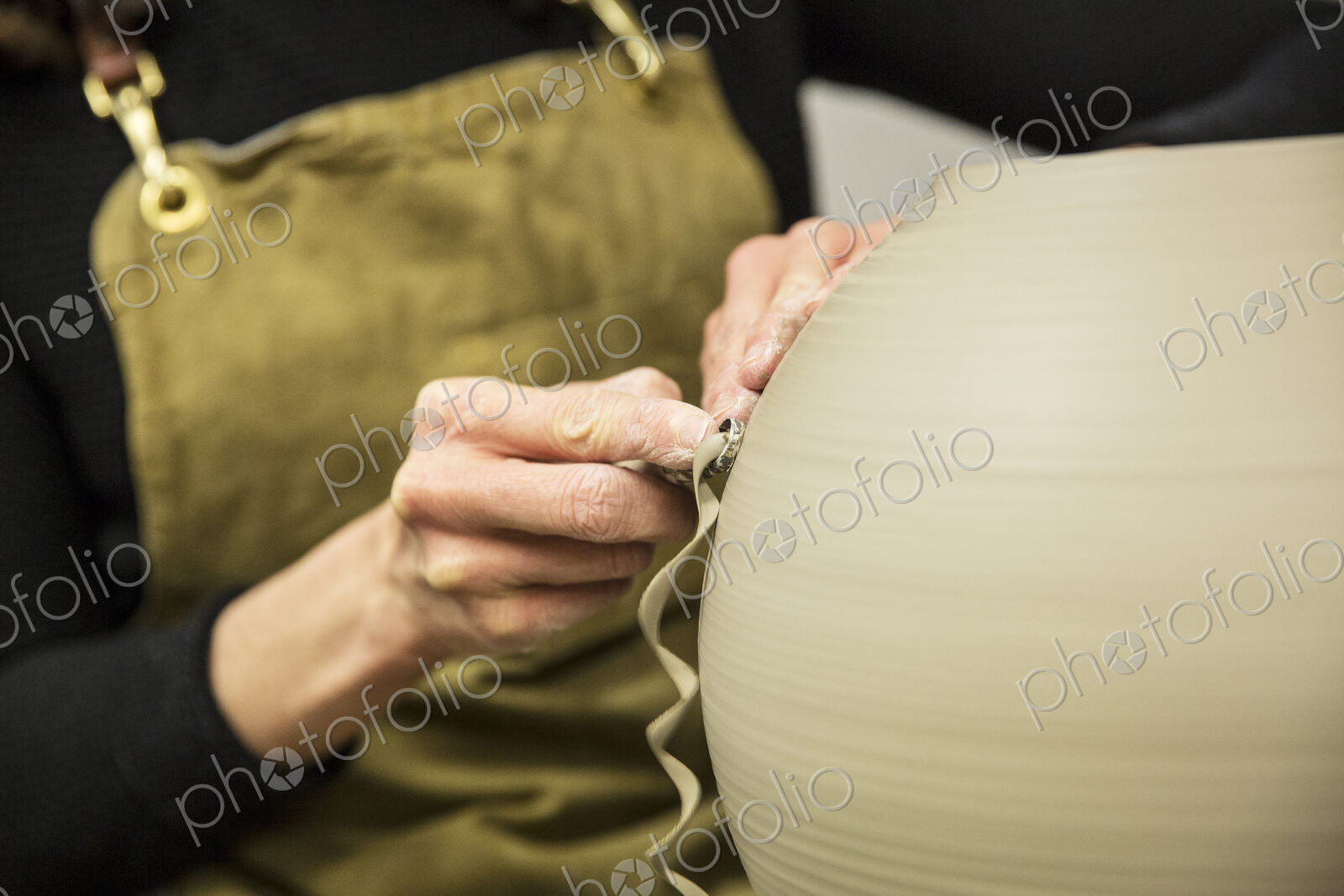 Close up of potter wearing apron working on spherical clay vase on pottery wheel.