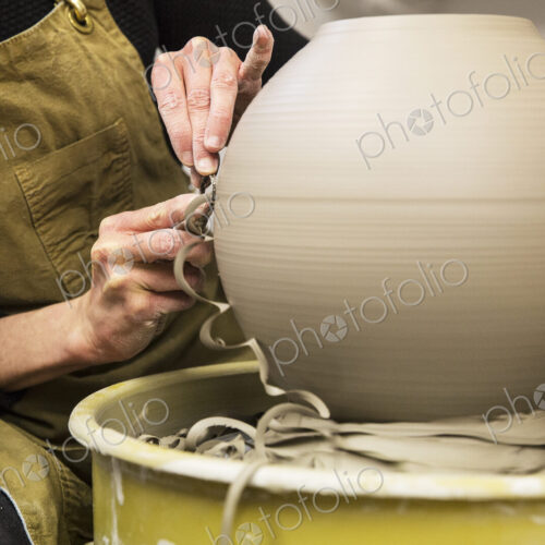 Close up of potter wearing apron working on spherical clay vase on pottery wheel. Close up of potter wearing apron working on spherical clay vase on pottery wheel.