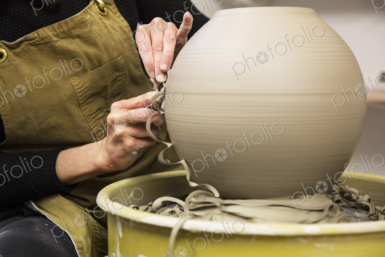 Close up of potter wearing apron working on spherical clay vase on pottery wheel.