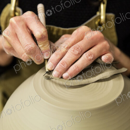 Close up of potter wearing apron working on spherical clay vase on pottery wheel. Close up of potter wearing apron working on spherical clay vase on pottery wheel.