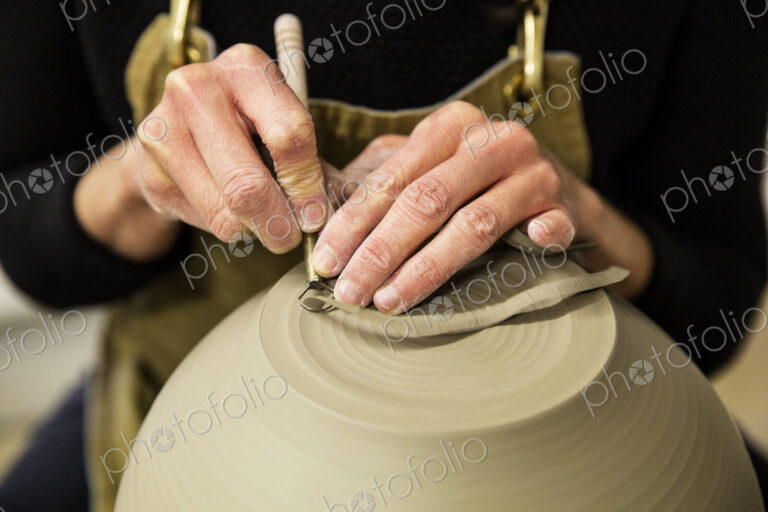 Close up of potter wearing apron working on spherical clay vase on pottery wheel.