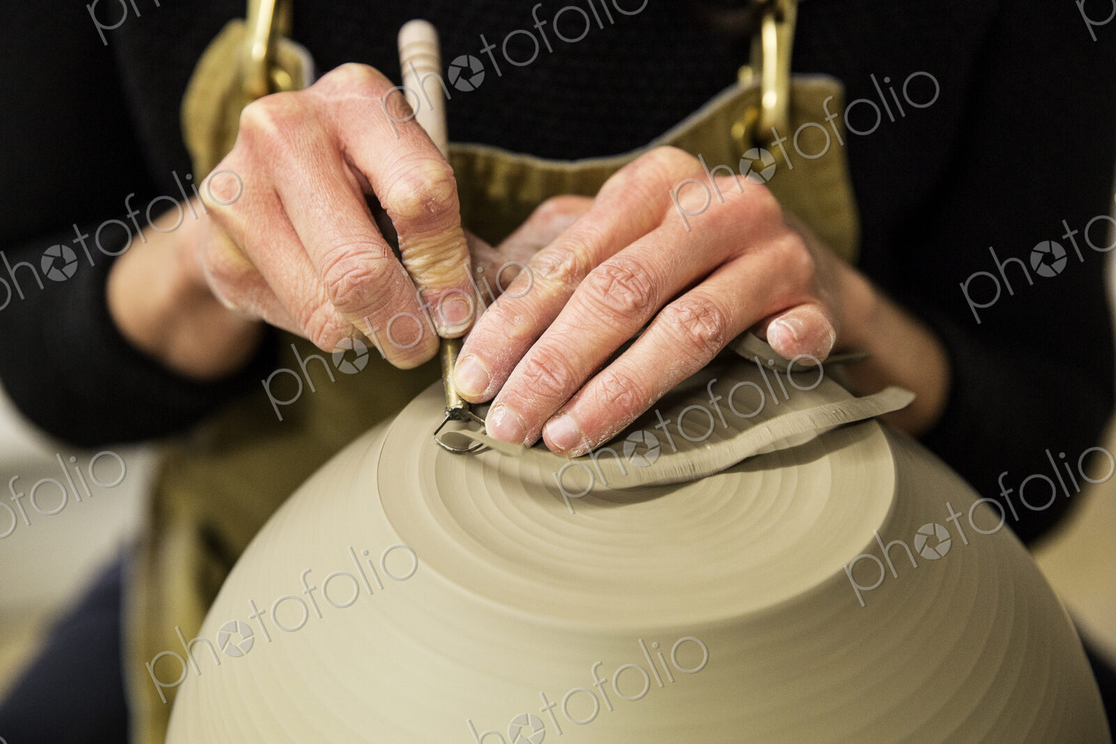 Close up of potter wearing apron working on spherical clay vase on pottery wheel.