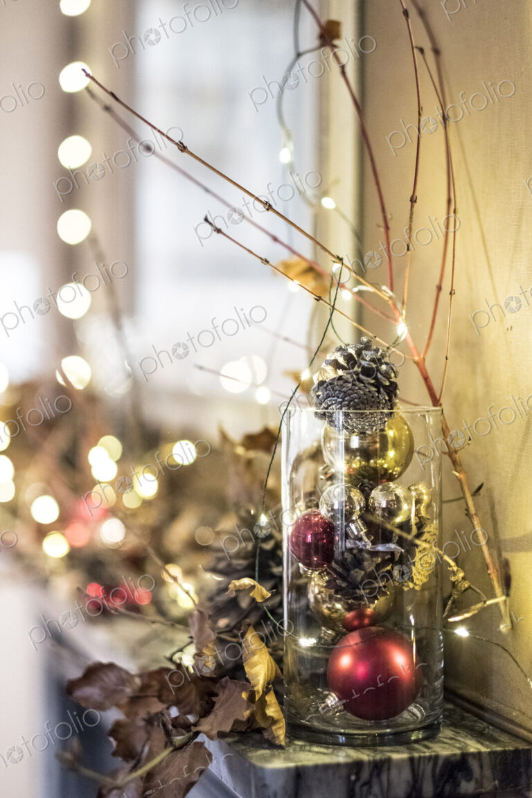 Close up of red and golden Christmas decorations in a vase, bauble, leaves and twigs.
