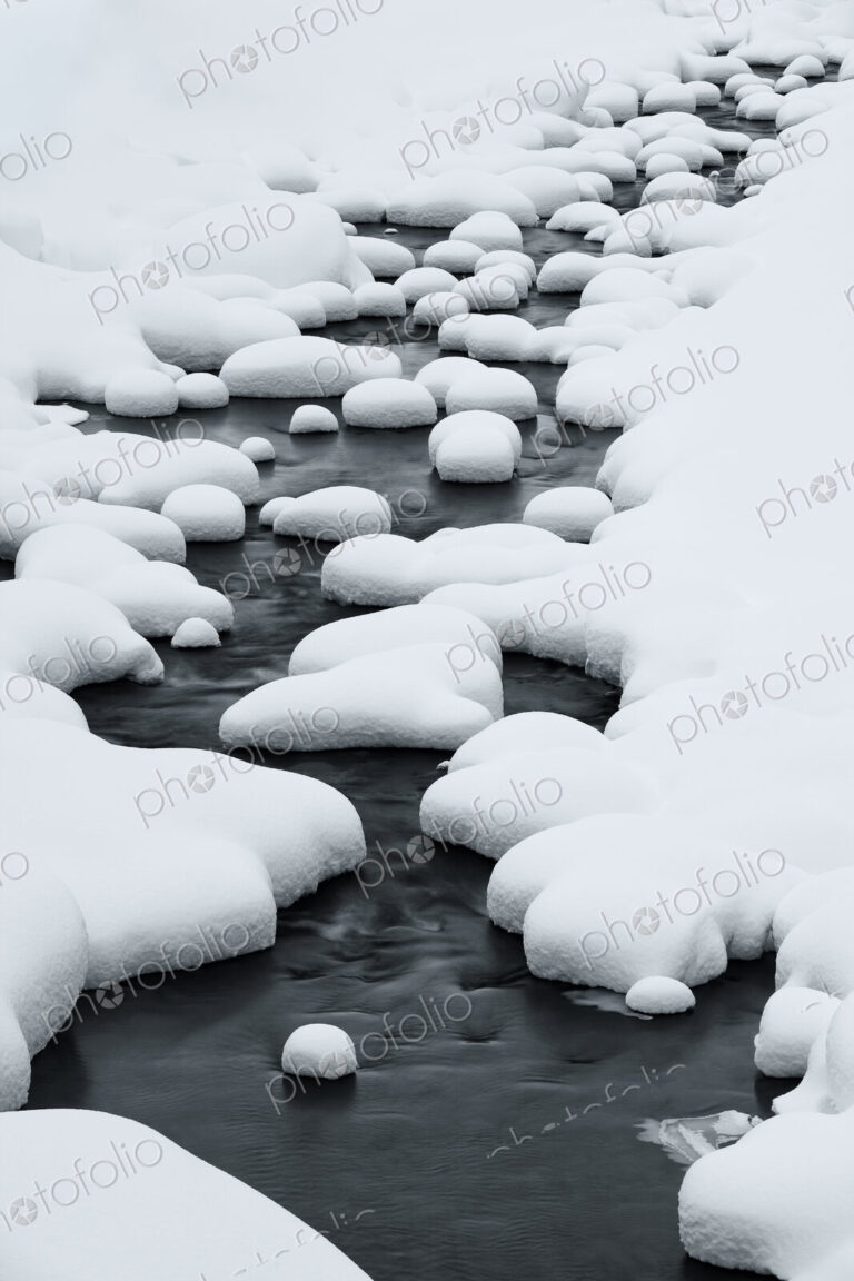 Close up of riverbed with snow-covered rocks in winter.